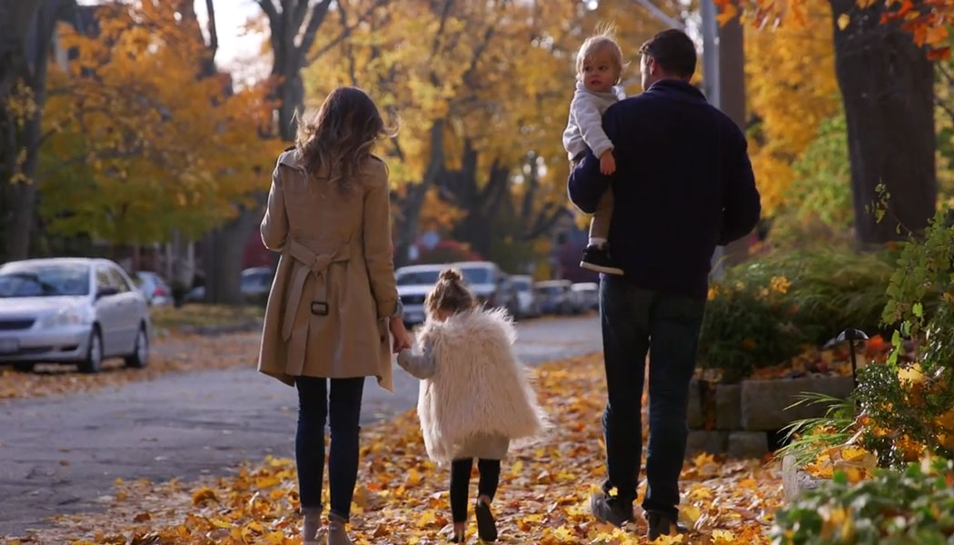 Family on sidewalk with fall leaves on the ground.
