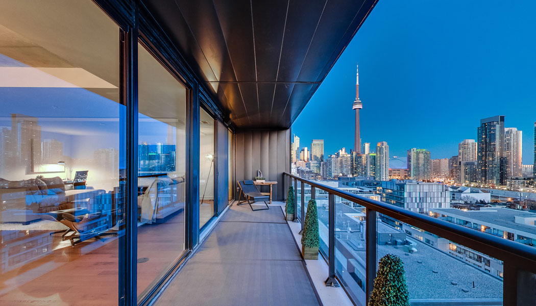 Condo balcony with night time view of the city and the CN Tower in Toronto.