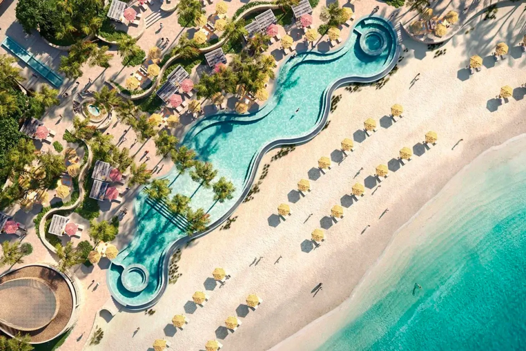 Top-down view of Vie L'Ven's luxury meandering pool by the beach, dotted with umbrellas and loungers, on the sands of St. Maarten.