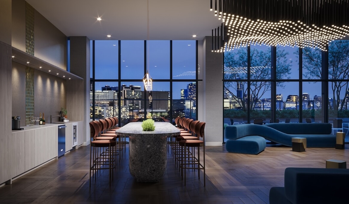 A modern bar and lounge interior at night with sleek furniture, a kitchenette, and large windows overlooking a cityscape.