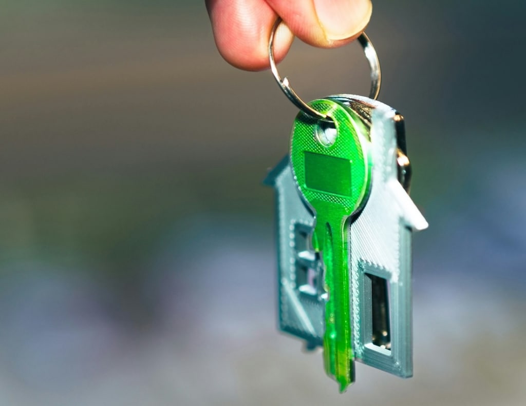 A hand holding a green key with a house shaped keychain