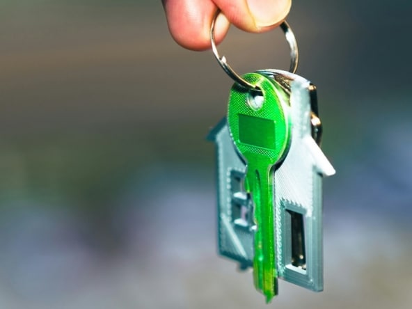 A hand holding a green key with a house shaped keychain